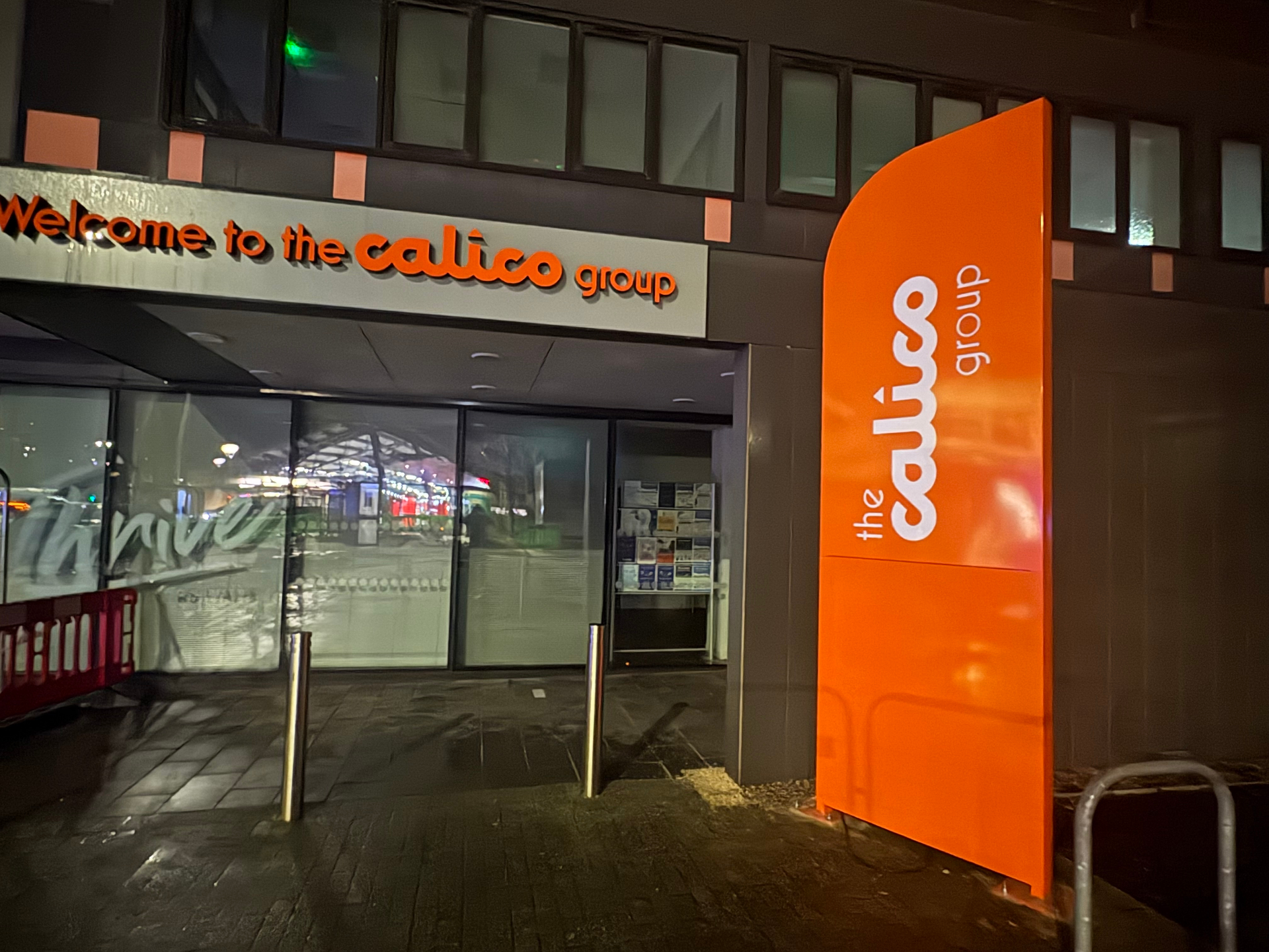 Illuminated orange Calico Group totem sign at the building entrance at night